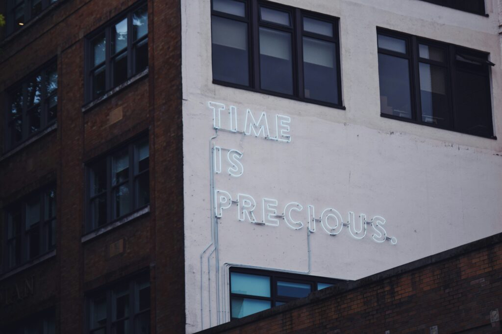 The corner of a building. On one side a neon sign spells out the words: Time is precious.