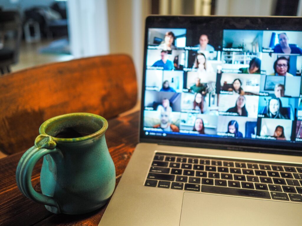 A desk with an open laptop showing a screen of multiple people in little squares - It's a networking event. Next to the laptop is a coffee mug. 